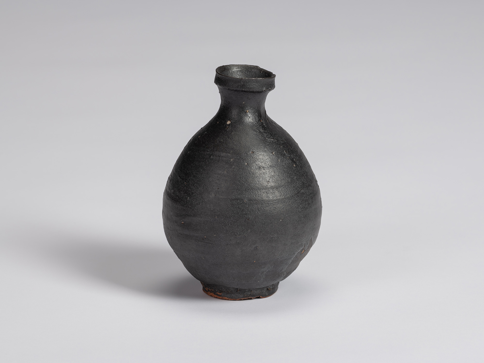Kuro Tokkuri by Shiro Tsujimura, with a full oval body, short narrow neck, and irregular flared...