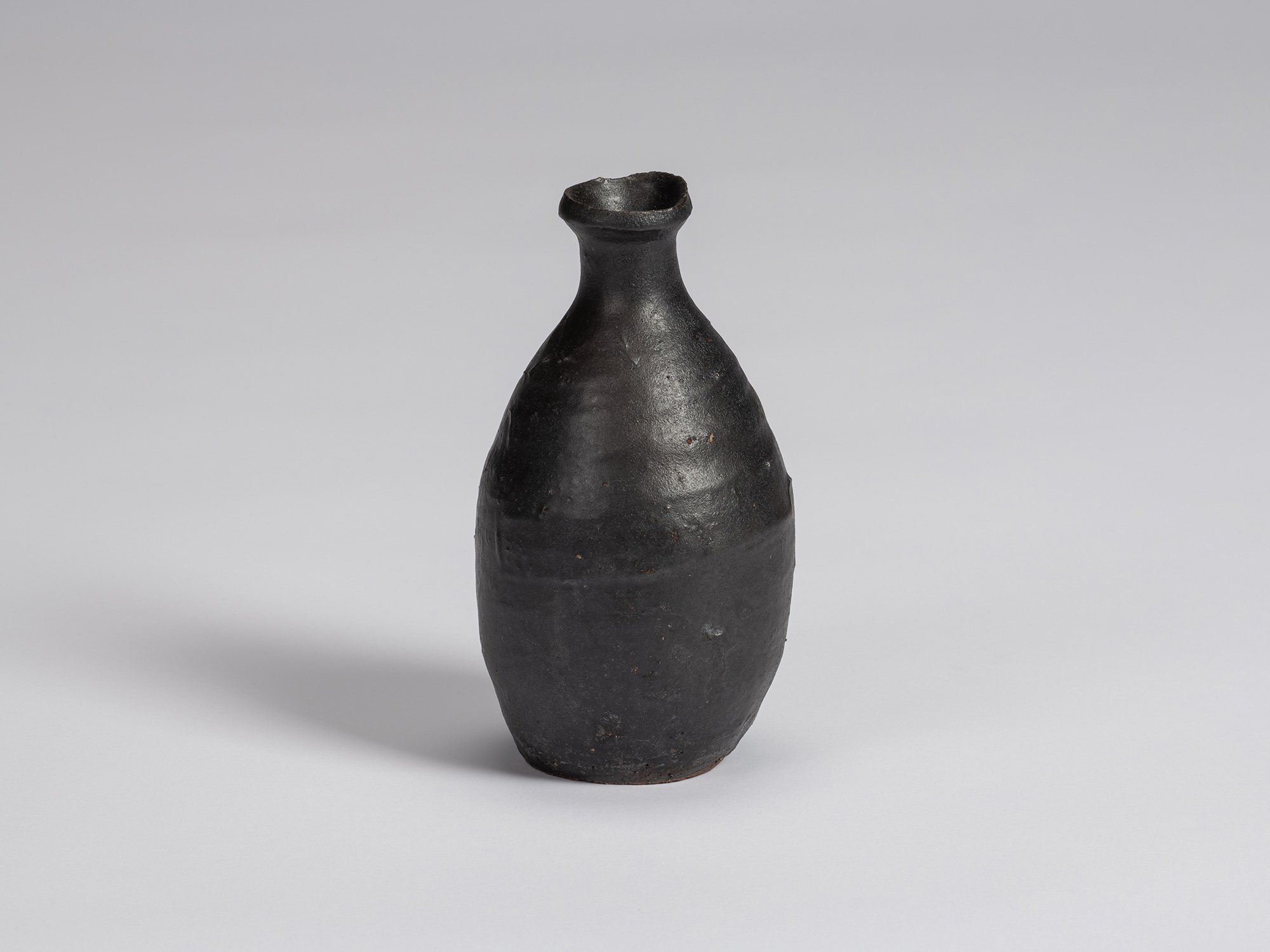 Kuro Tokkuri by Shiro Tsujimura, with an elongated oval body, narrow neck, and irregular flared...