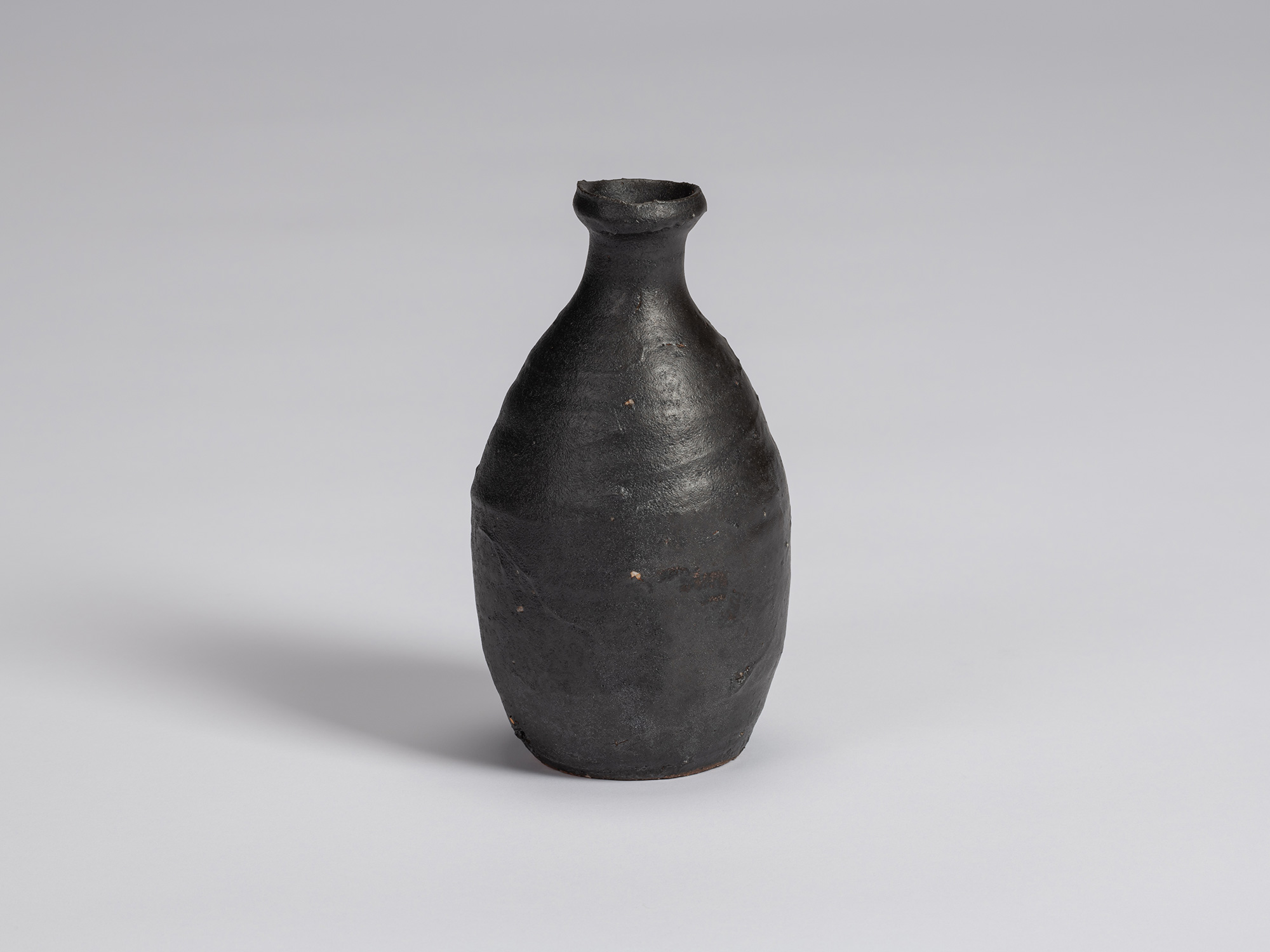 Kuro Tokkuri by Shiro Tsujimura, with an elongated oval body, narrow neck, and irregular flared...