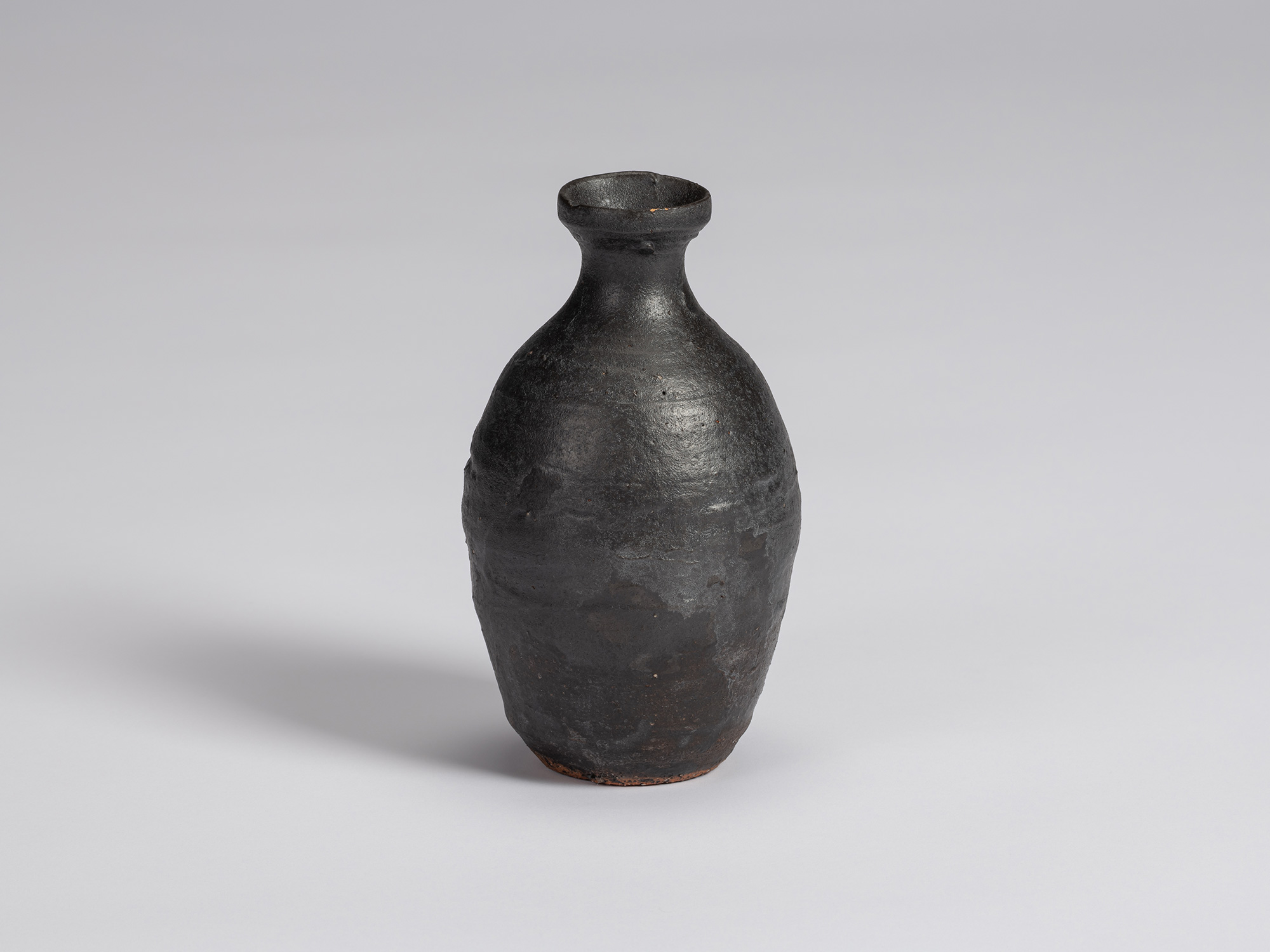 Kuro Tokkuri by Shiro Tsujimura, with a tall rounded body, narrow neck, and irregular flared rim....