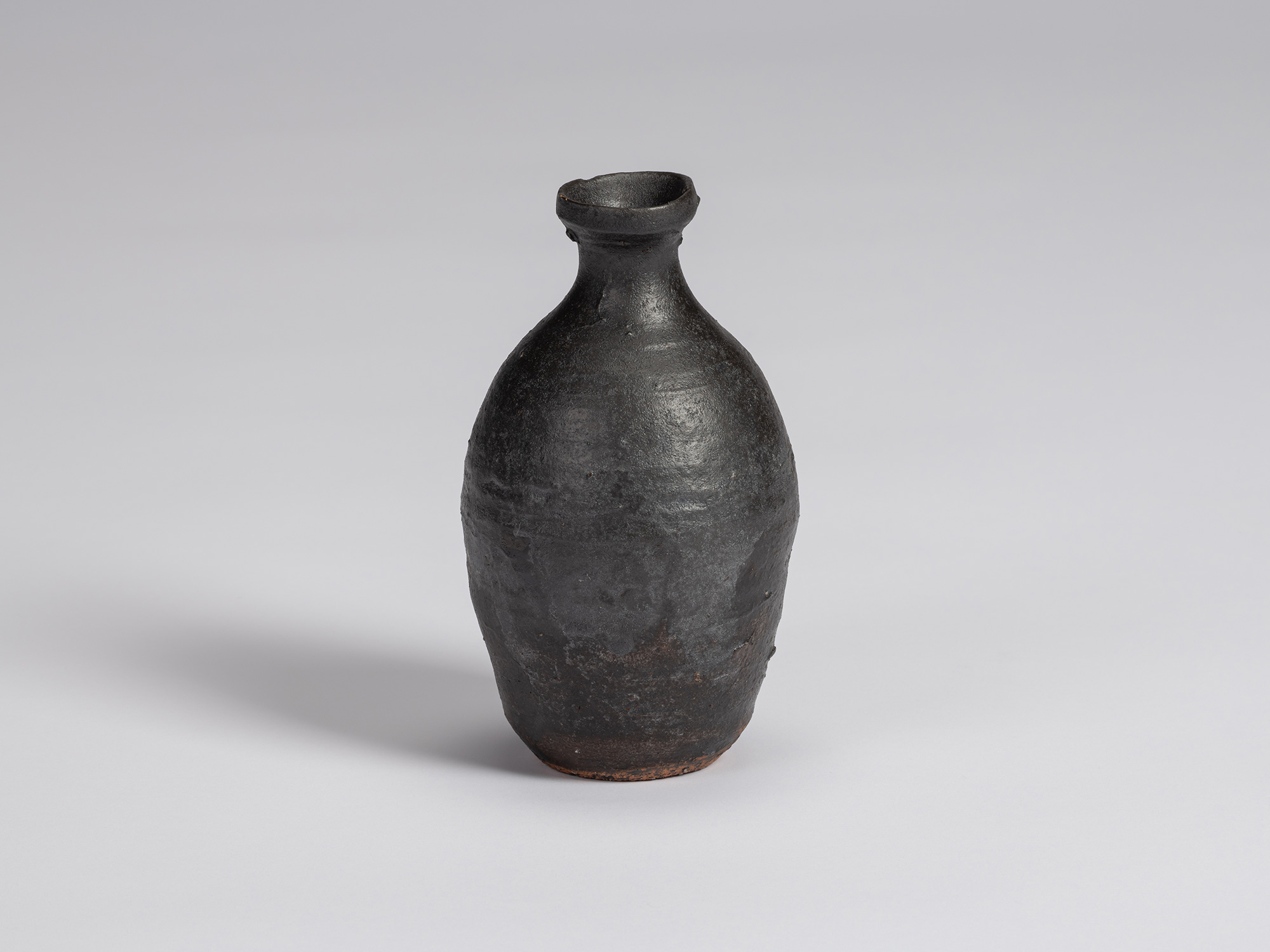 Kuro Tokkuri by Shiro Tsujimura, with a tall rounded body, narrow neck, and irregular flared rim....