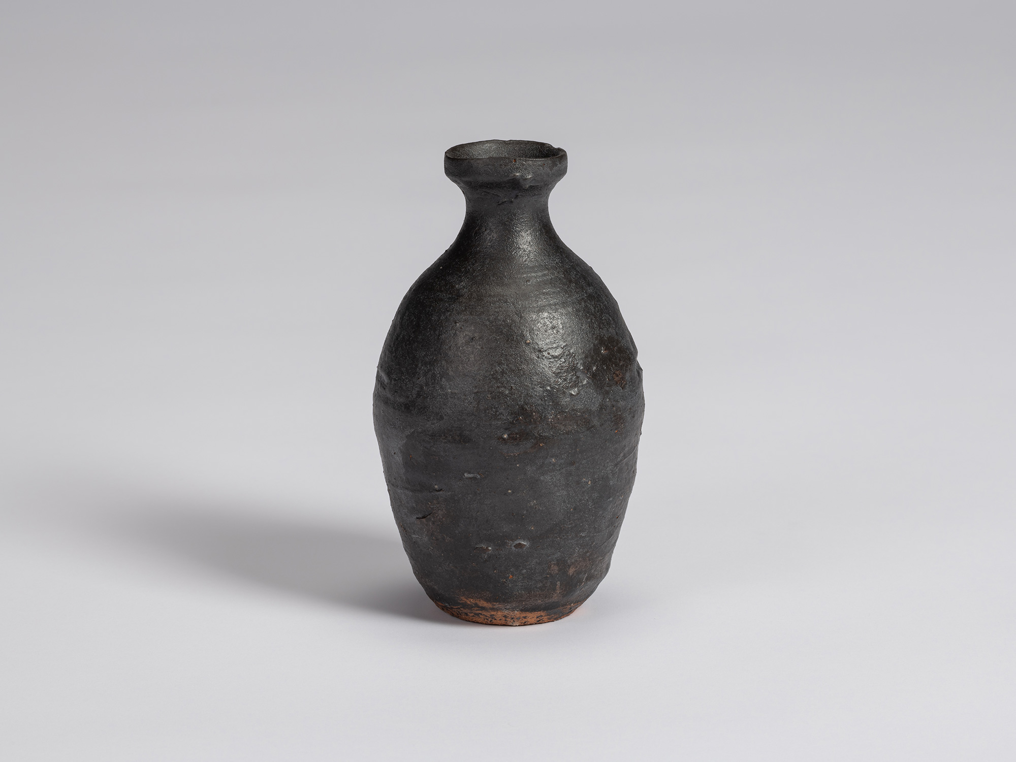 Kuro Tokkuri by Shiro Tsujimura, with a tall rounded body, narrow neck, and irregular flared rim....