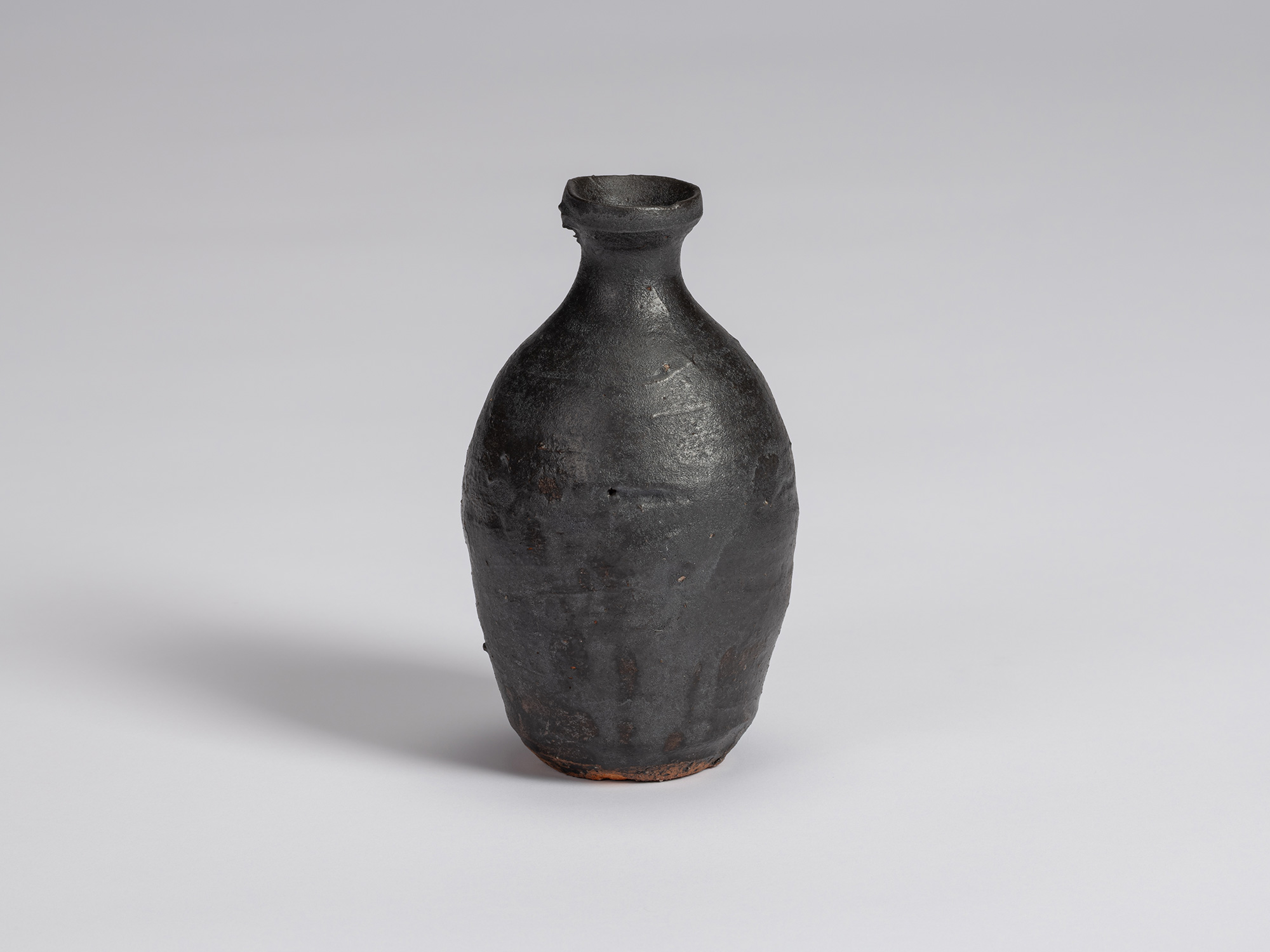 Kuro Tokkuri by Shiro Tsujimura, with a tall rounded body, narrow neck, and irregular flared rim....