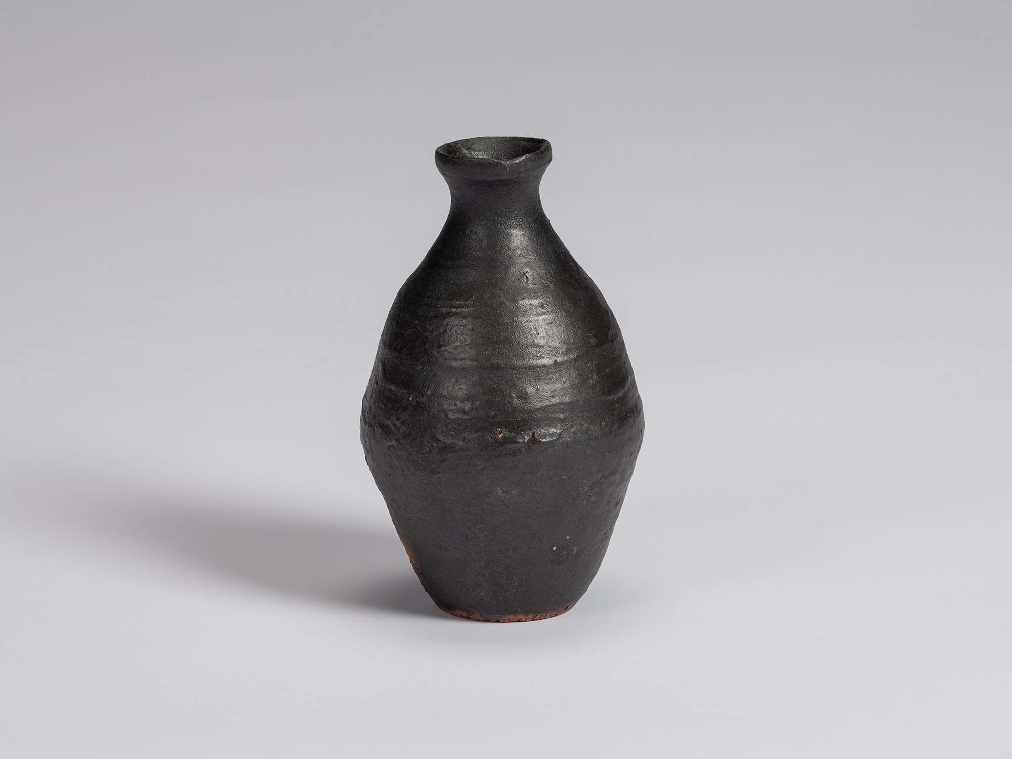 Kuro Tokkuri by Shiro Tsujimura, with an elongated rounded body, narrow neck, and irregular flared...