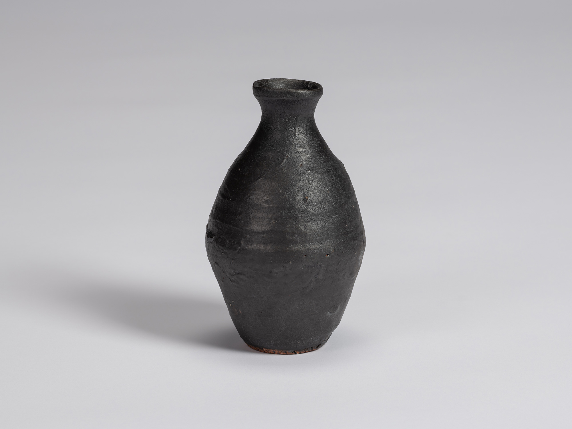 Kuro Tokkuri by Shiro Tsujimura, with an elongated rounded body, narrow neck, and irregular flared...