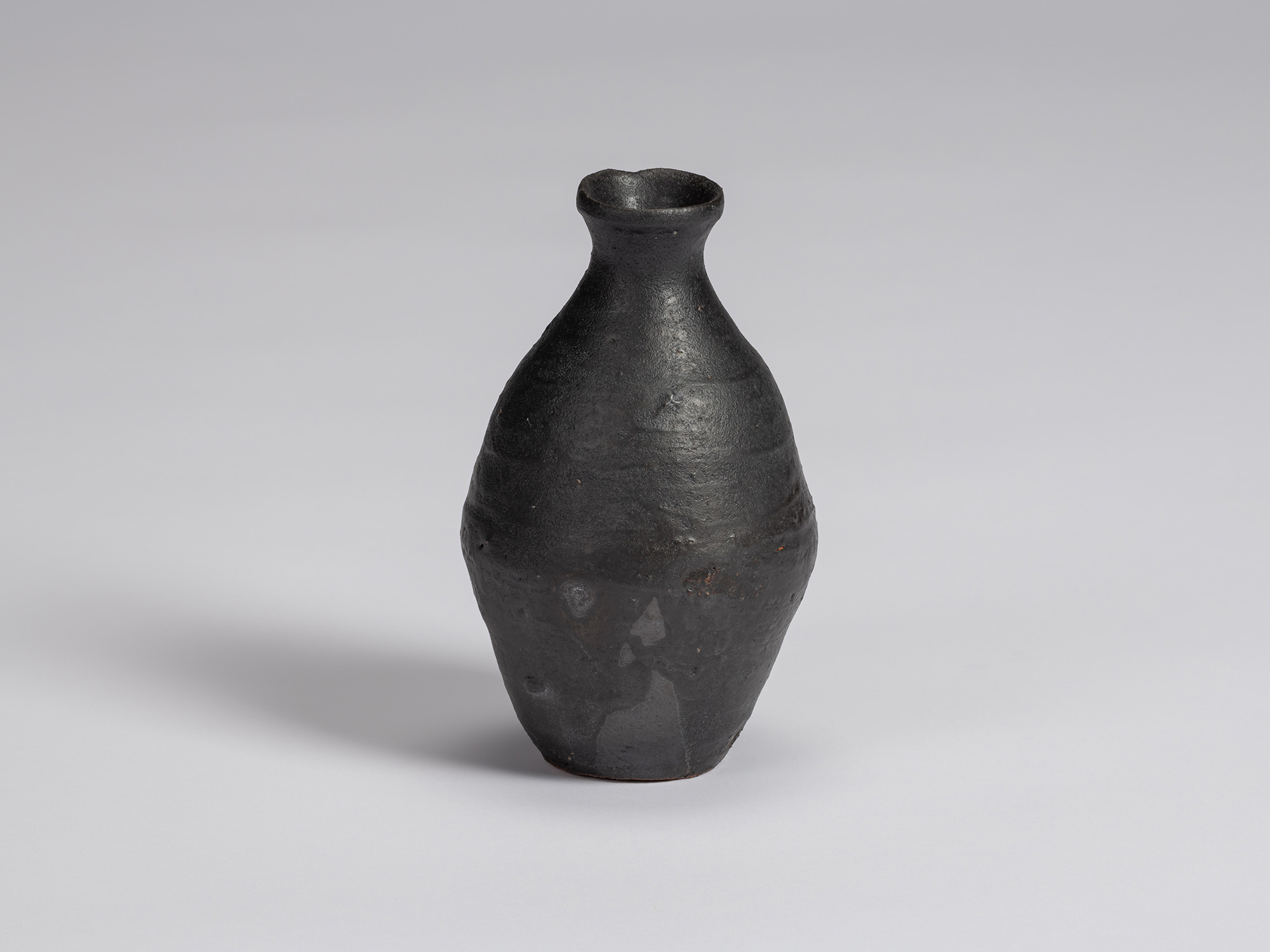 Kuro Tokkuri by Shiro Tsujimura, with an elongated rounded body, narrow neck, and irregular flared...