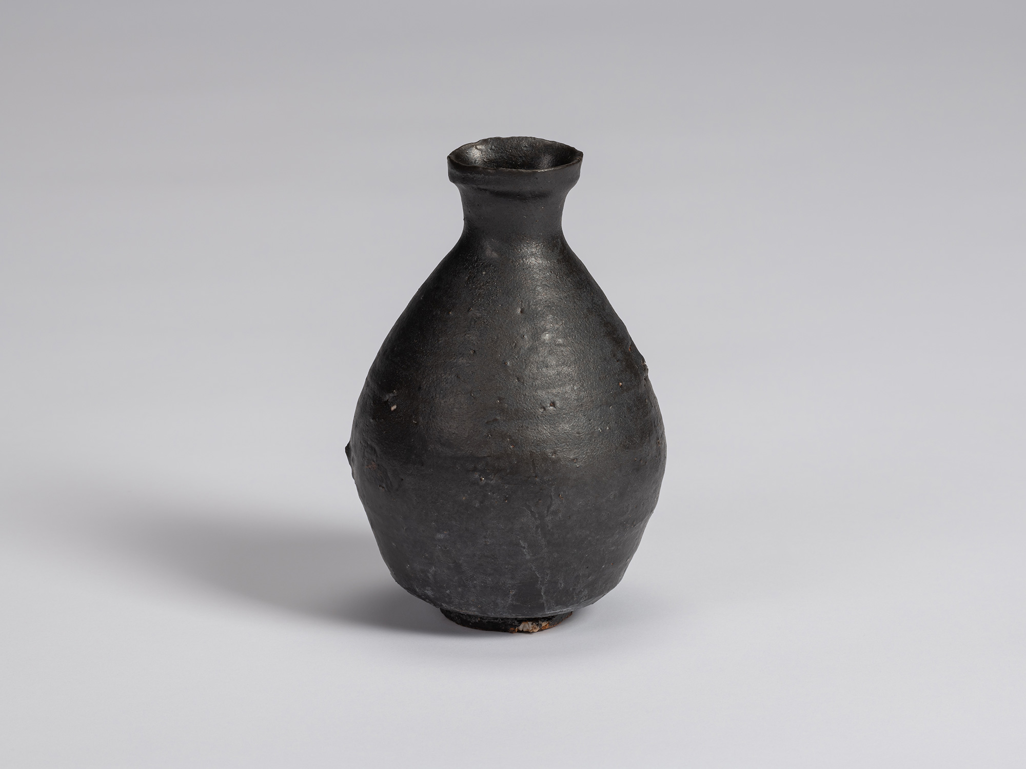 Kuro Tokkuri by Shiro Tsujimura, with a broad rounded body, narrow neck, and irregular flared rim....