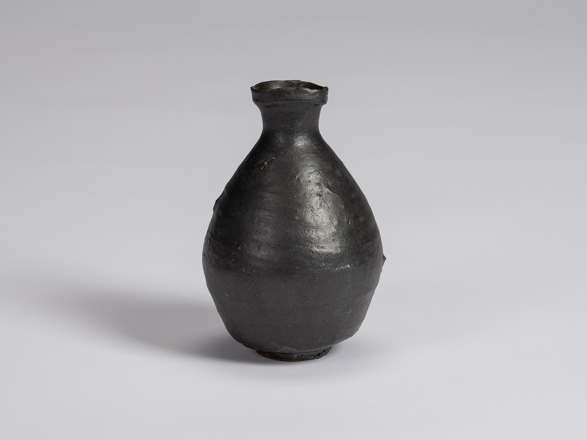 Kuro Tokkuri by Shiro Tsujimura, with a broad rounded body, narrow neck, and irregular flared rim....