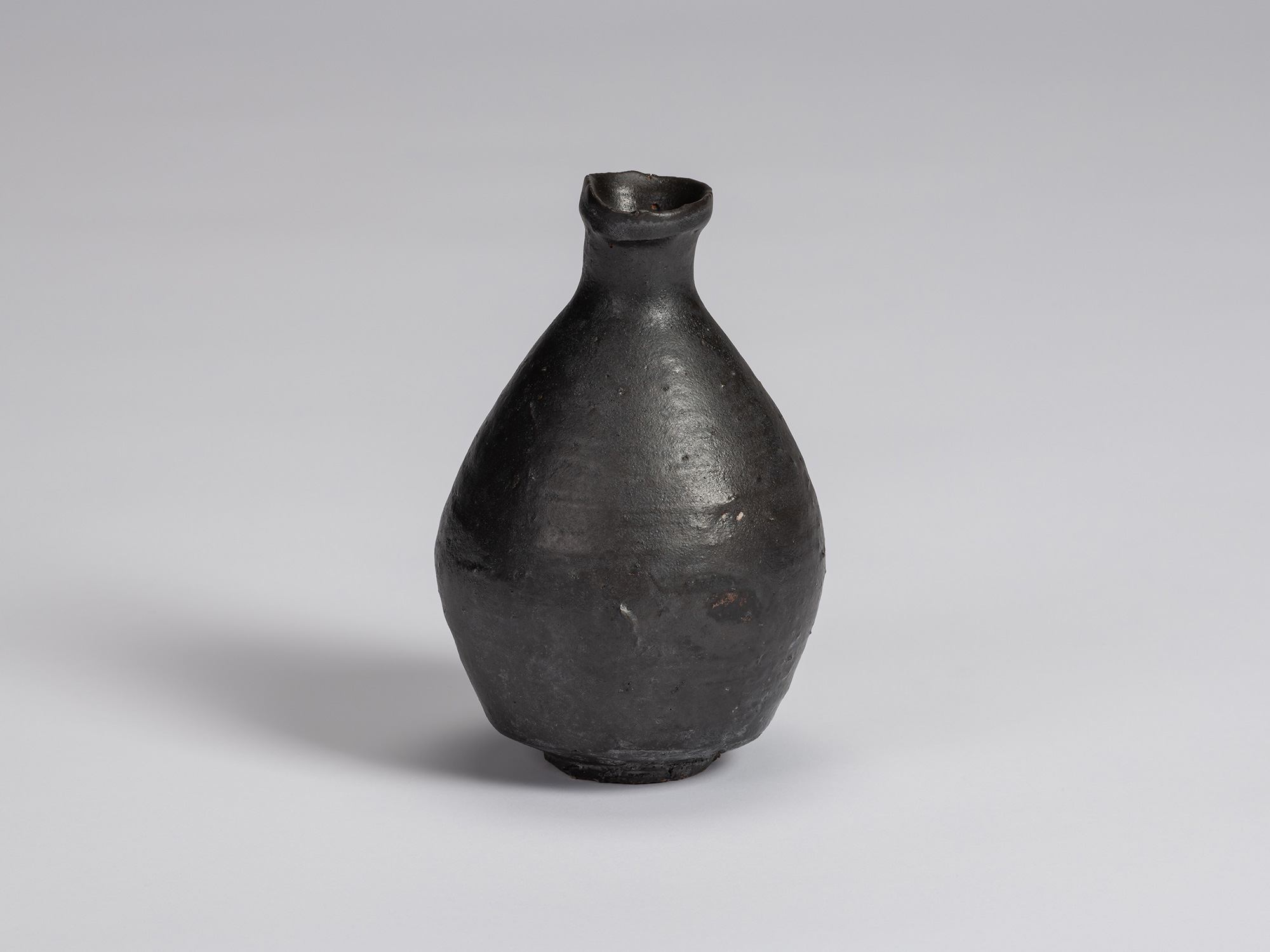 Kuro Tokkuri by Shiro Tsujimura, with a broad rounded body, narrow neck, and irregular flared rim....