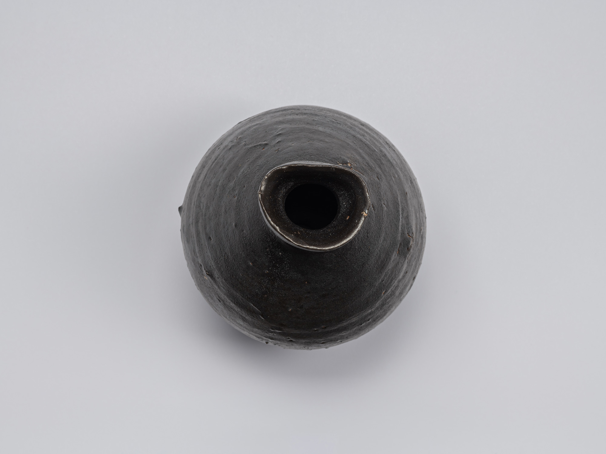 Overhead view of the Kuro Tokkuri by Shiro Tsujimura, showing the irregular oval mouth, thick uneven...
