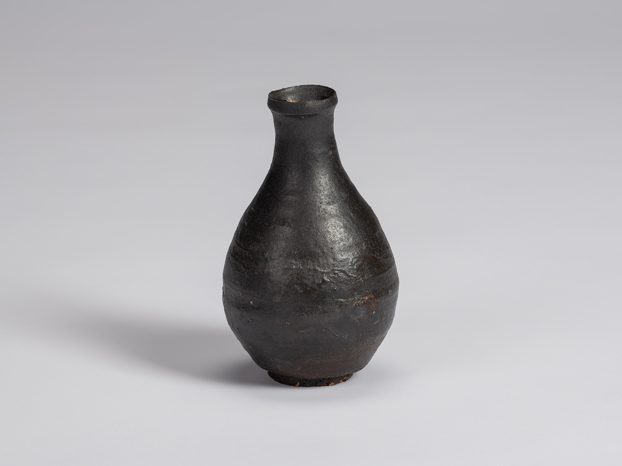 Kuro Tokkuri by Shiro Tsujimura, with a tall pear-shaped body, narrow neck, and irregular flared...