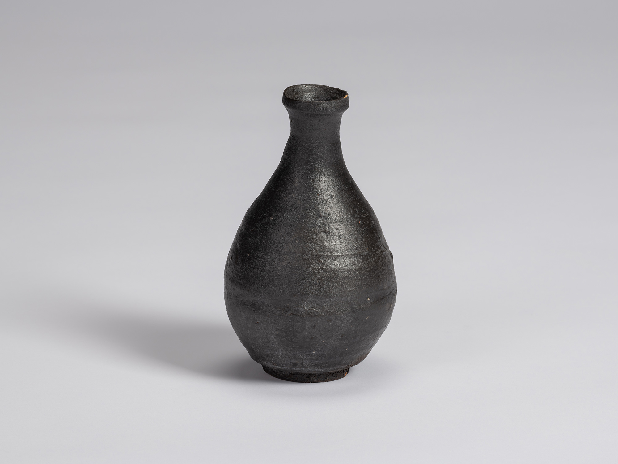 Kuro Tokkuri by Shiro Tsujimura, with a tall pear-shaped body, narrow neck, and irregular flared...