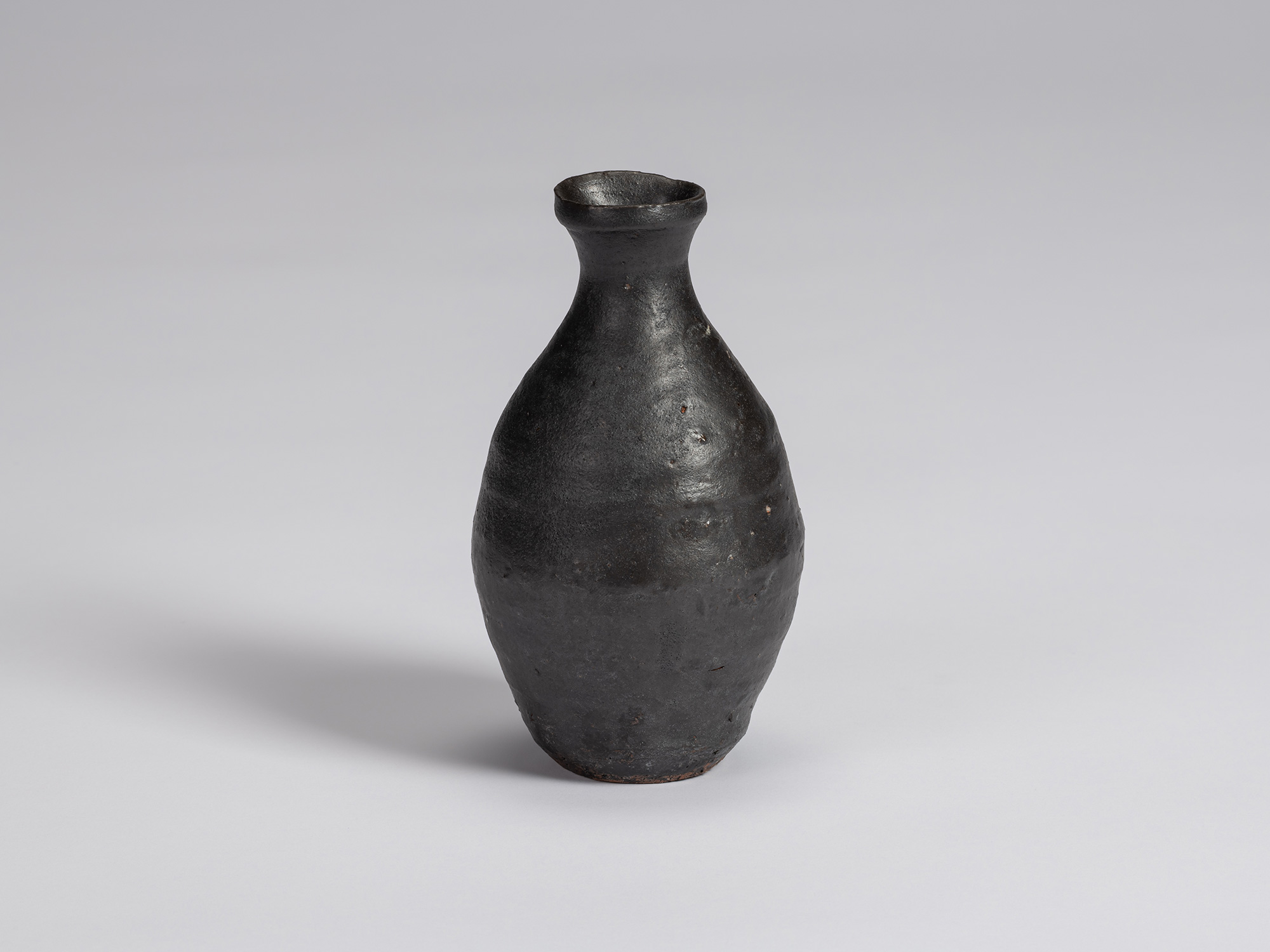 Kuro Tokkuri by Shiro Tsujimura, with a tall oval body, narrow neck, and irregular flared rim....