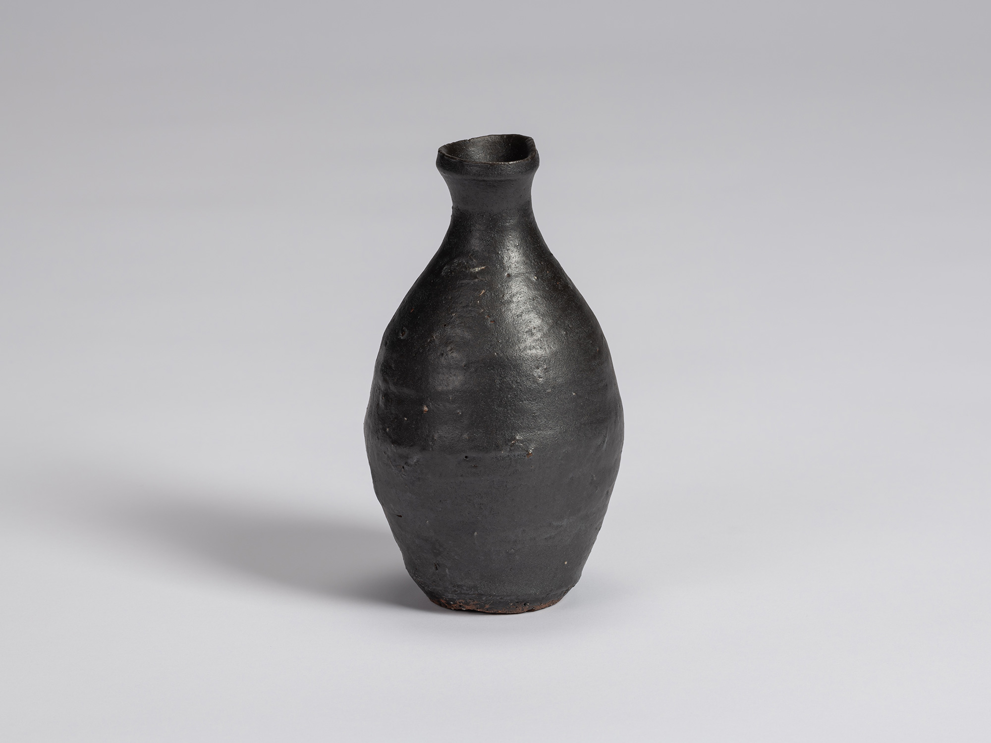Kuro Tokkuri by Shiro Tsujimura, with a tall oval body, narrow neck, and irregular flared rim....