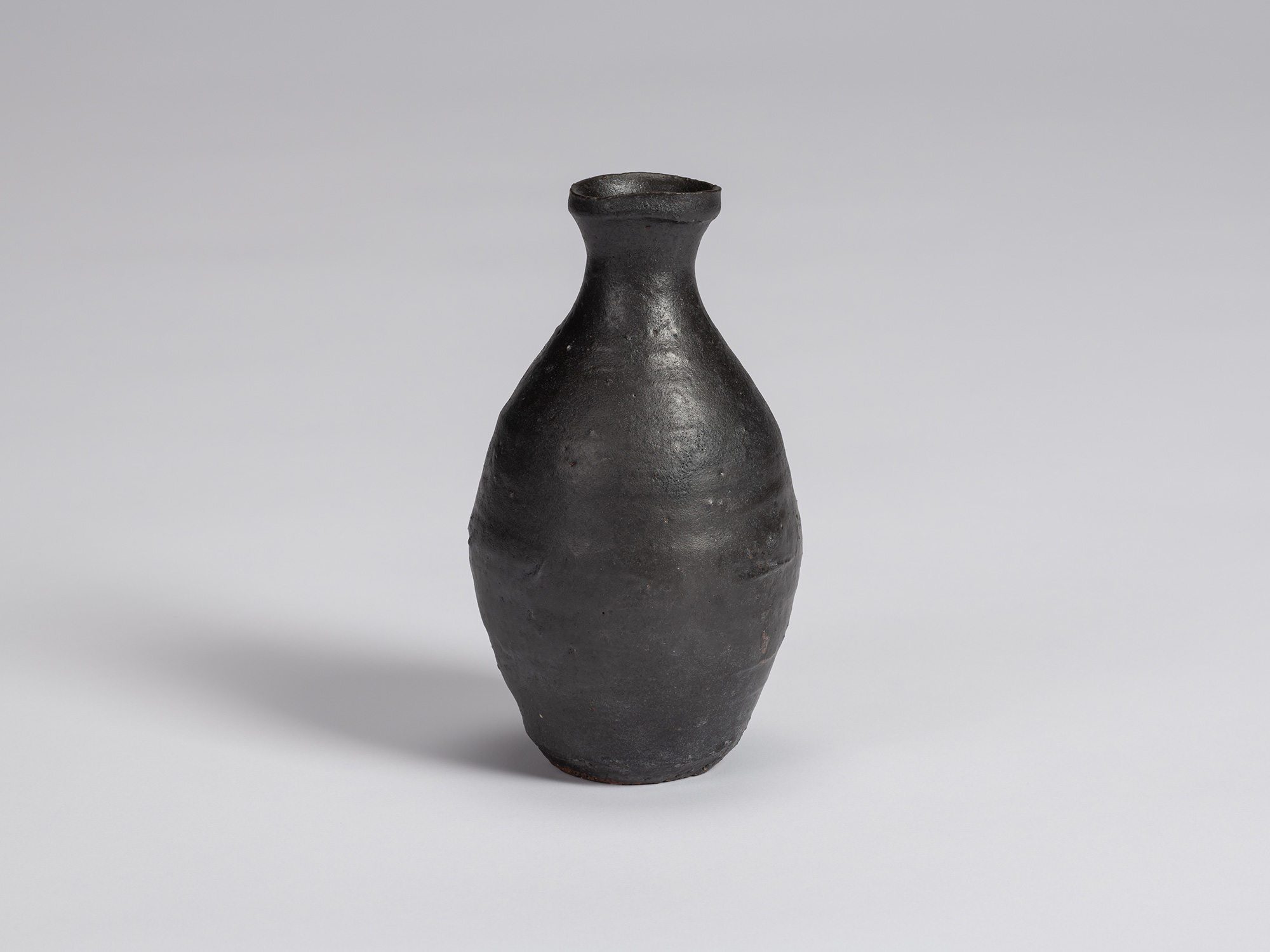 Kuro Tokkuri by Shiro Tsujimura, with a tall oval body, narrow neck, and irregular flared rim....