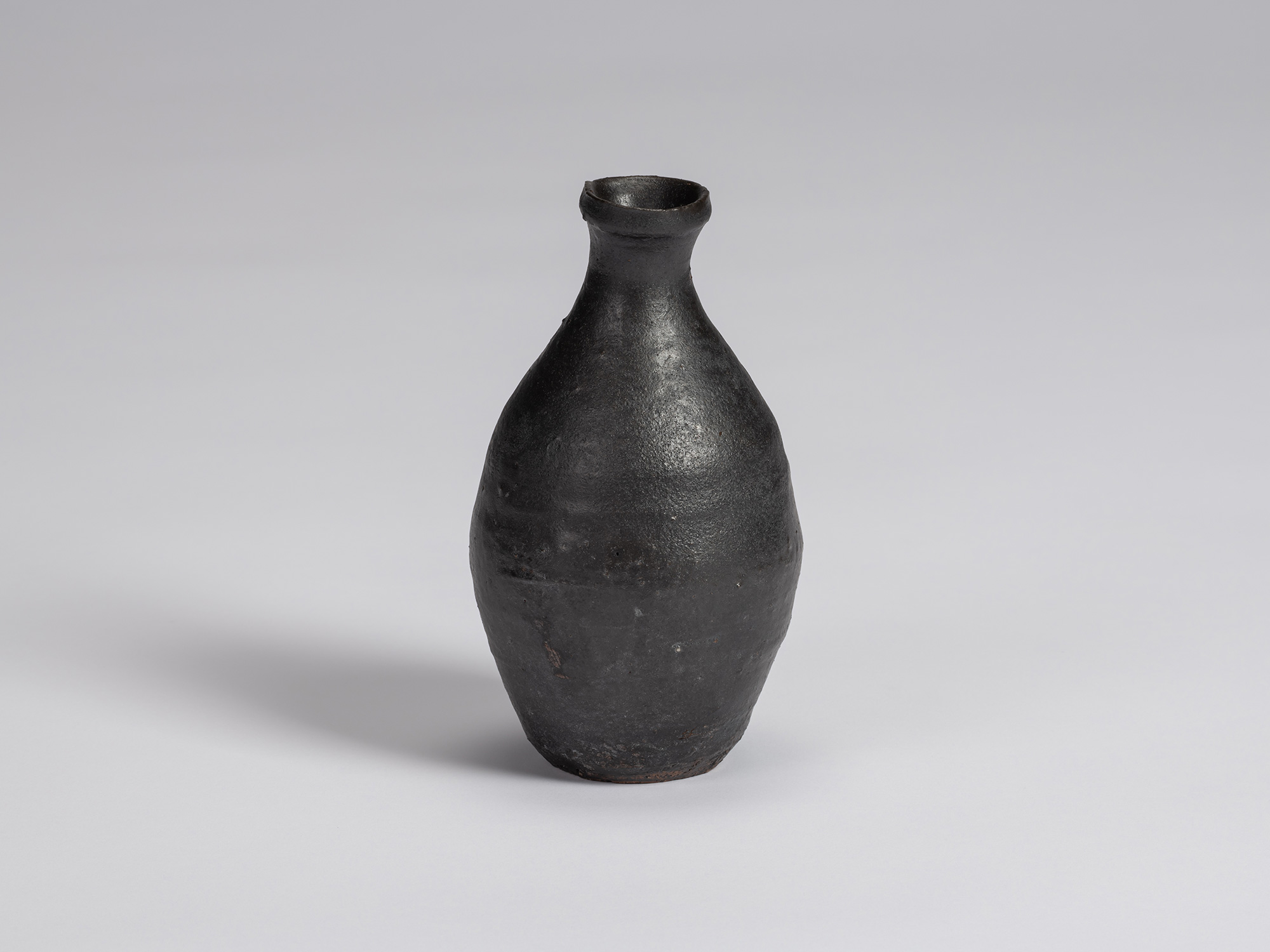 Kuro Tokkuri by Shiro Tsujimura, with a tall oval body, narrow neck, and irregular flared rim....