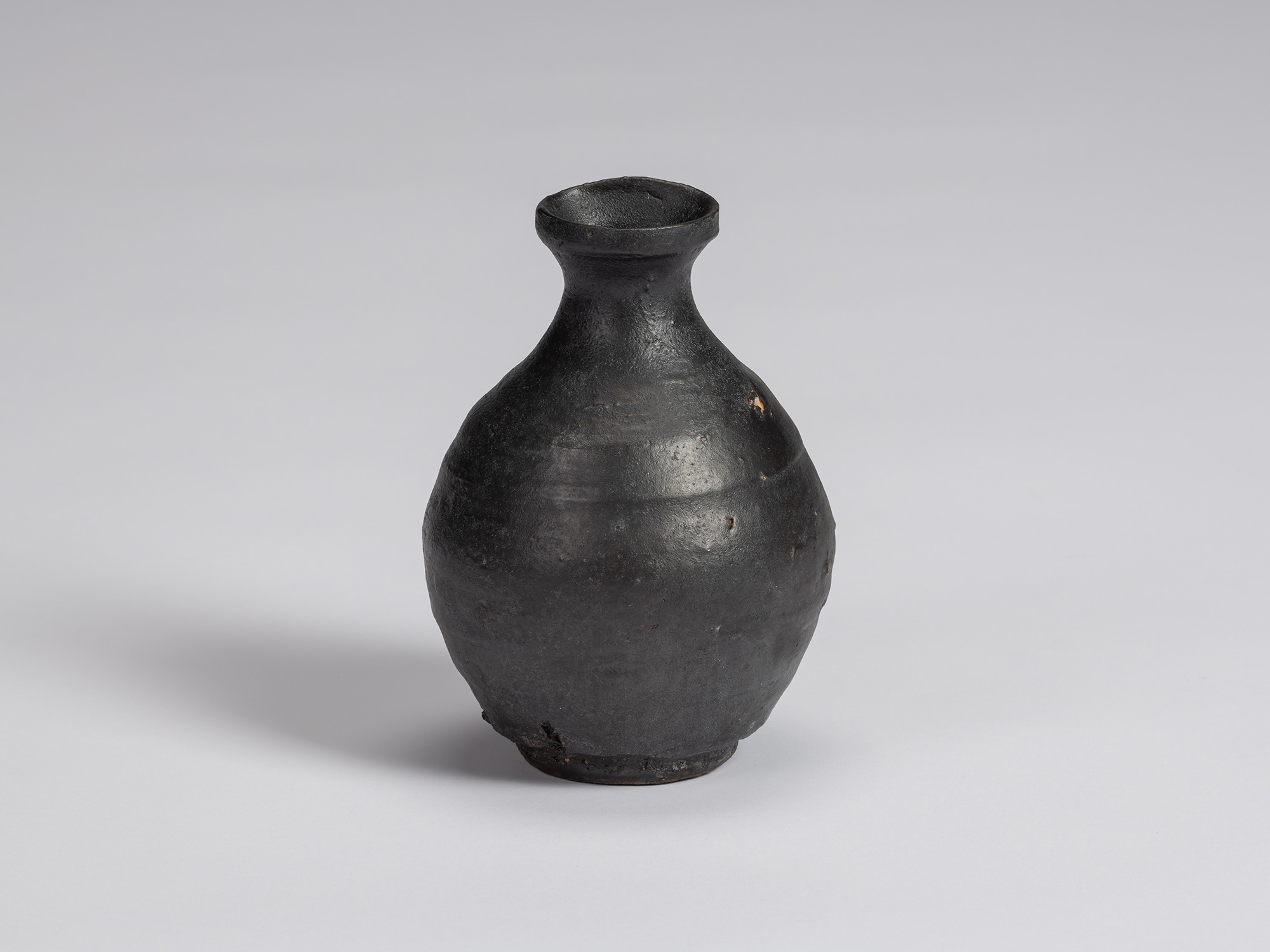 Kuro Tokkuri by Shiro Tsujimura with a rounded, slightly asymmetrical body, narrow neck, flared...