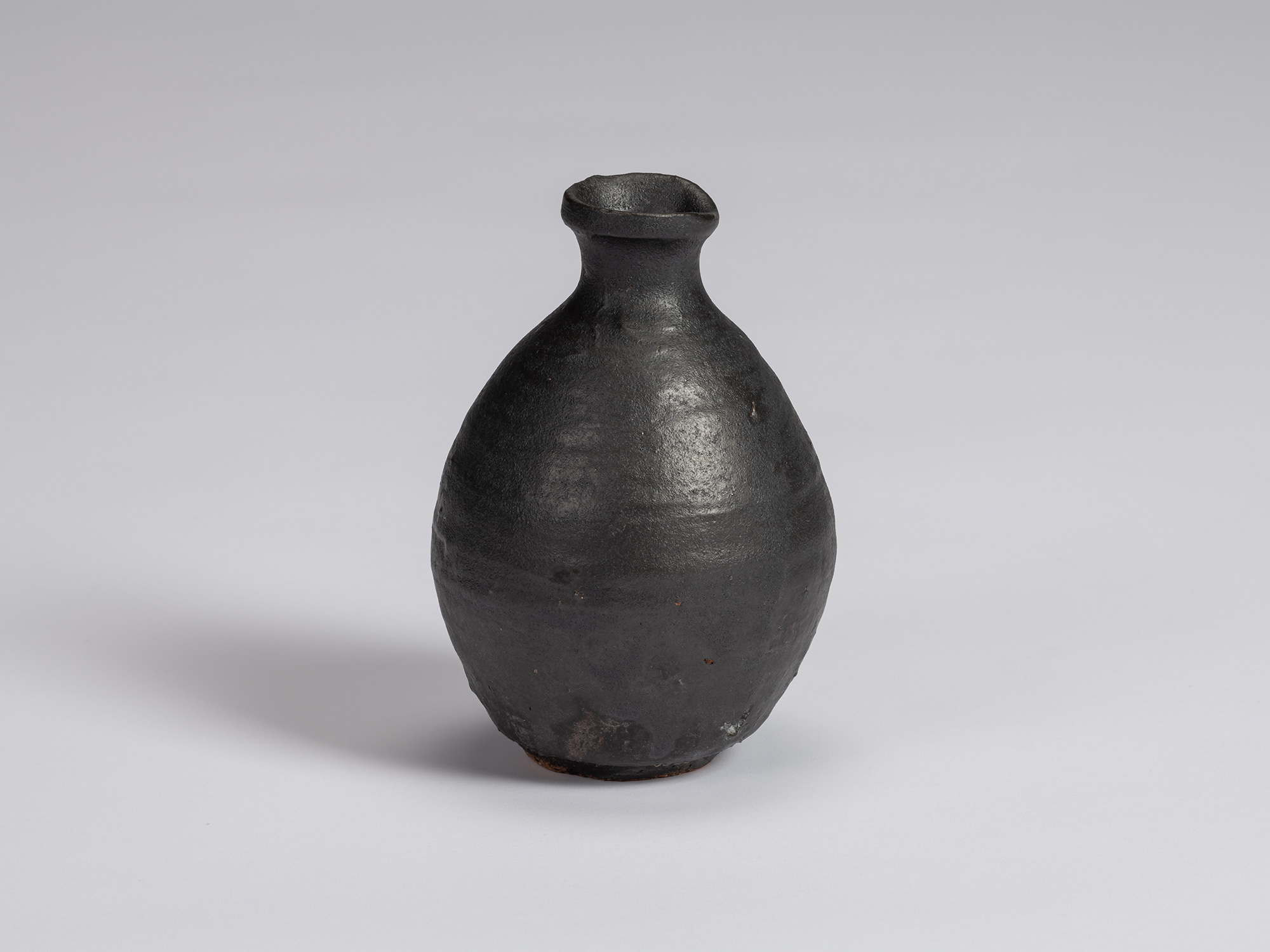 Kuro Tokkuri by Shiro Tsujimura with a rounded, slightly asymmetrical body, sloping shoulders,...