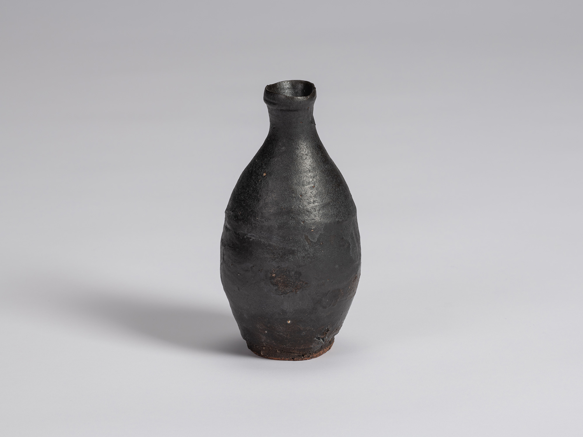 Kuro Tokkuri by Shiro Tsujimura, with a rounded, asymmetrical body, narrow neck, and irregular...