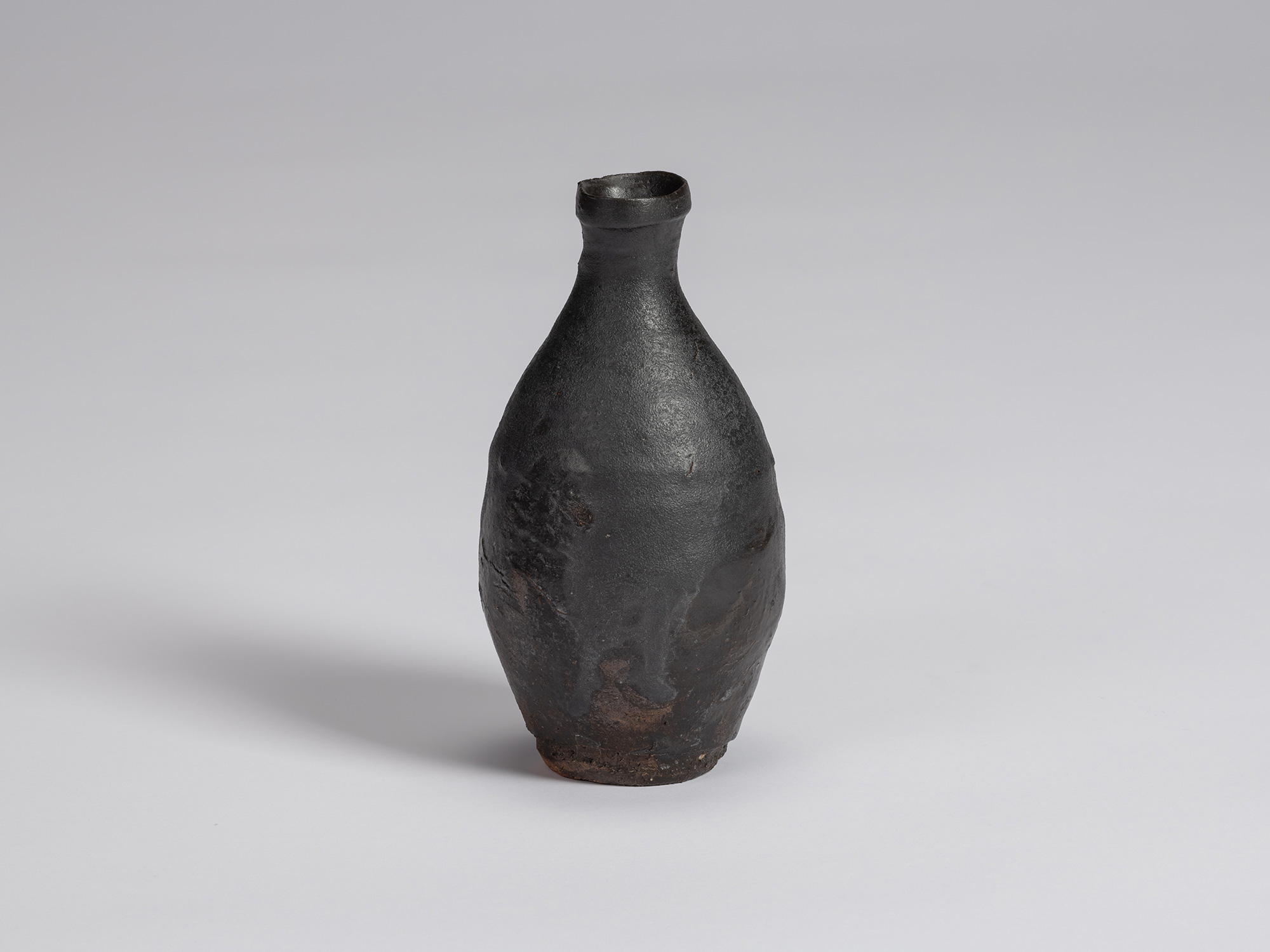 Kuro Tokkuri by Shiro Tsujimura, with a rounded, asymmetrical body, narrow neck, and irregular...