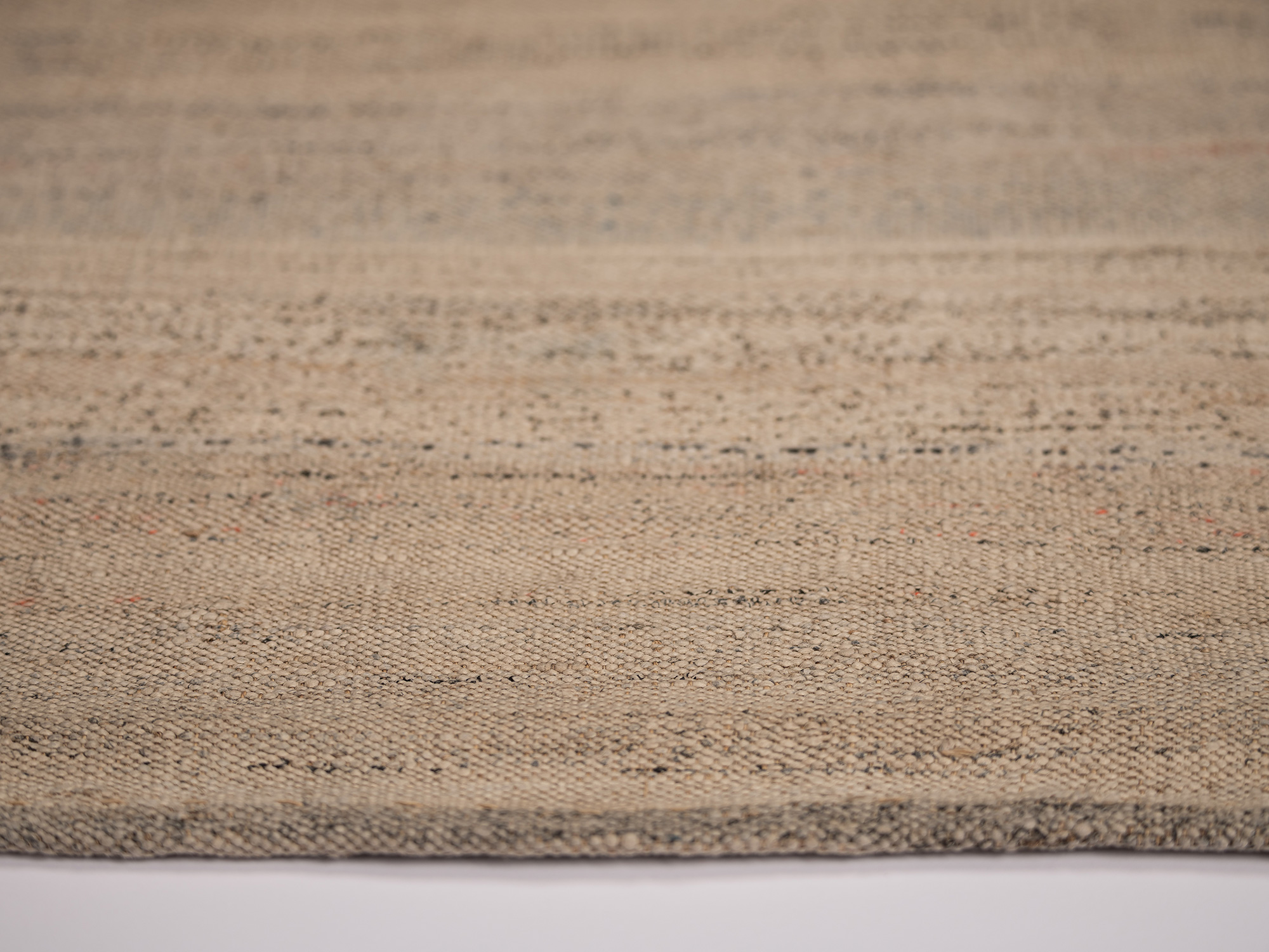 Detail view of otsuzure fabric showing a coarse, densely woven beige surface with irregular gray...