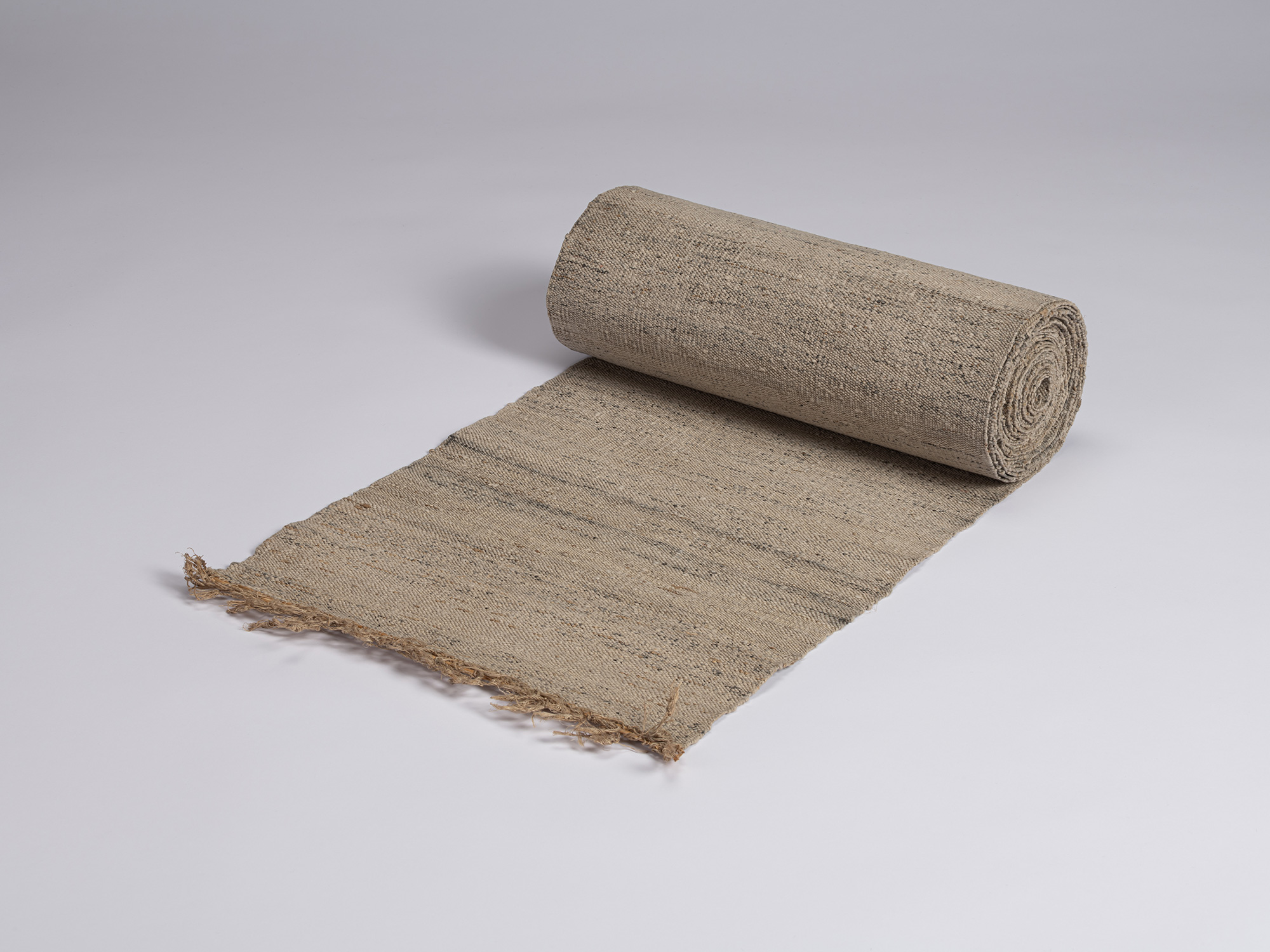Angled view of a partially unrolled bolt of undyed otsuzure, showing its narrow width, tightly...