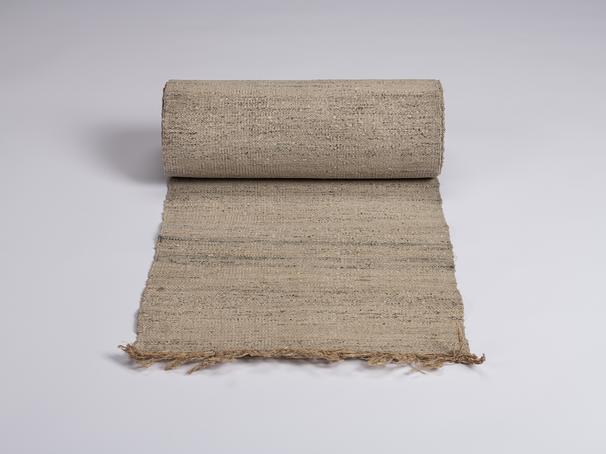 Partially unrolled bolt of undyed otsuzure fabric showing a coarse beige weave with irregular gray...