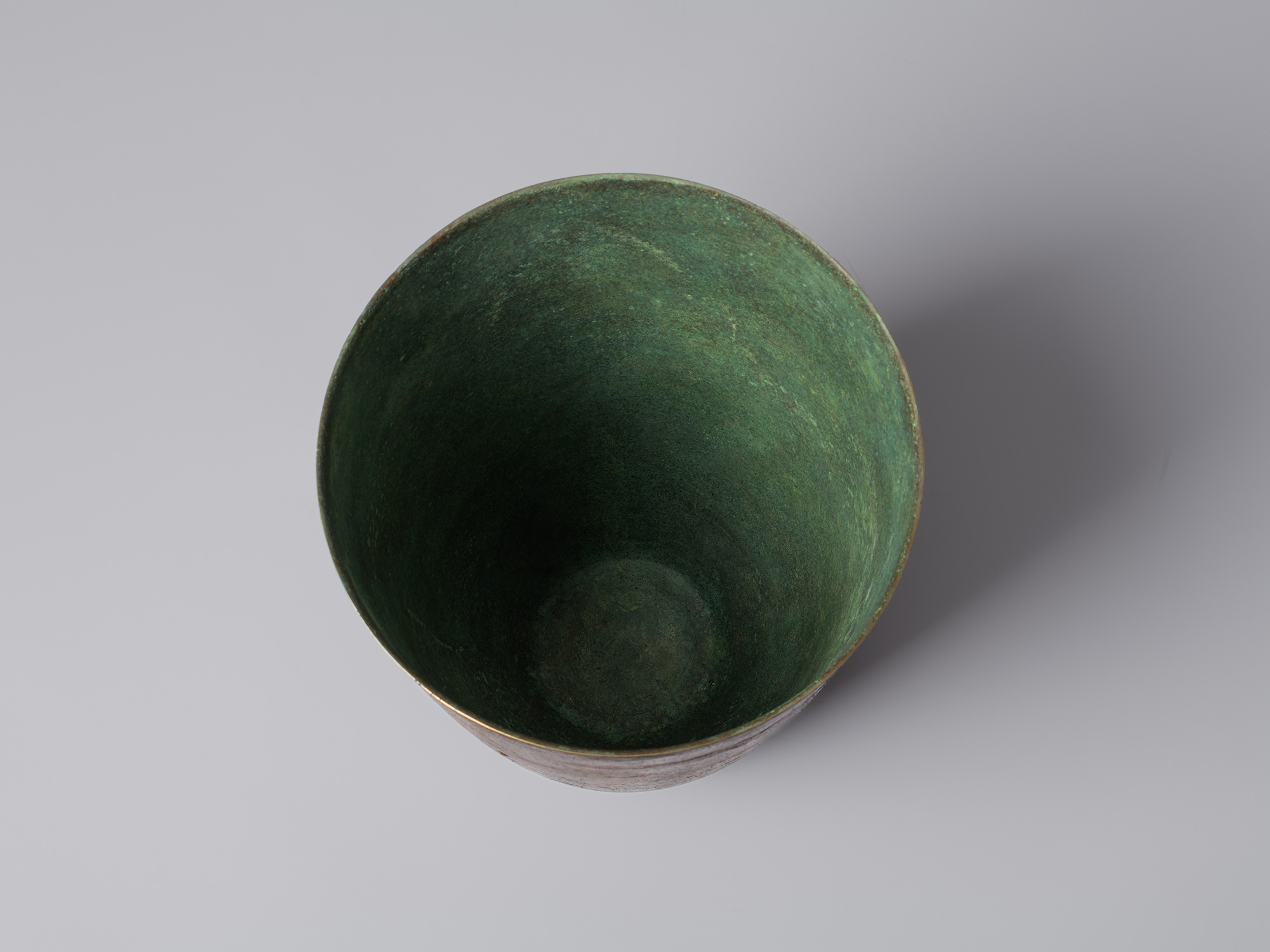 Overhead view of the bronze vessel, showing its circular opening and deep interior covered in mottled...