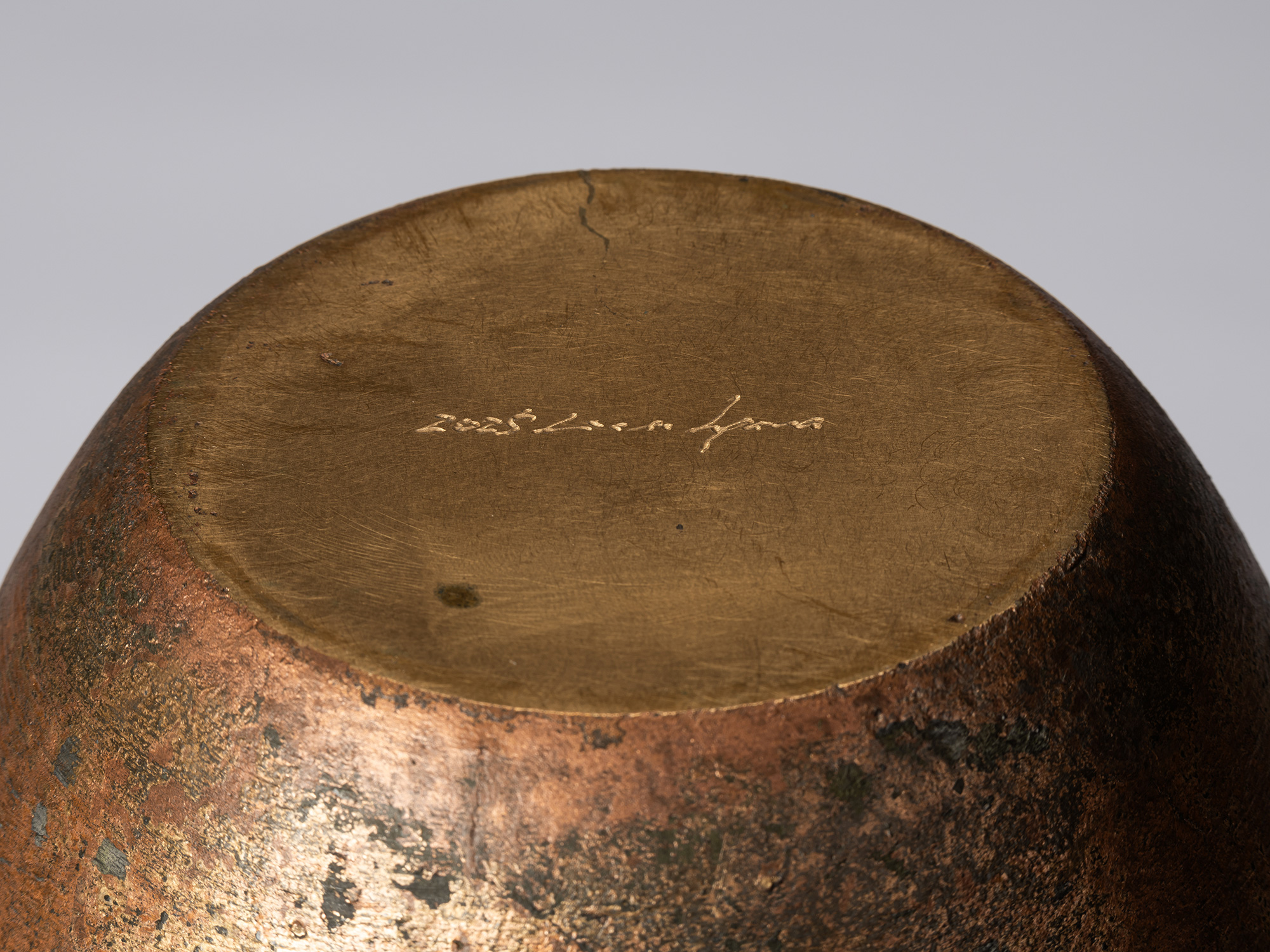 Detail of the underside of the bronze vessel, showing a smooth circular gold-toned base with the...