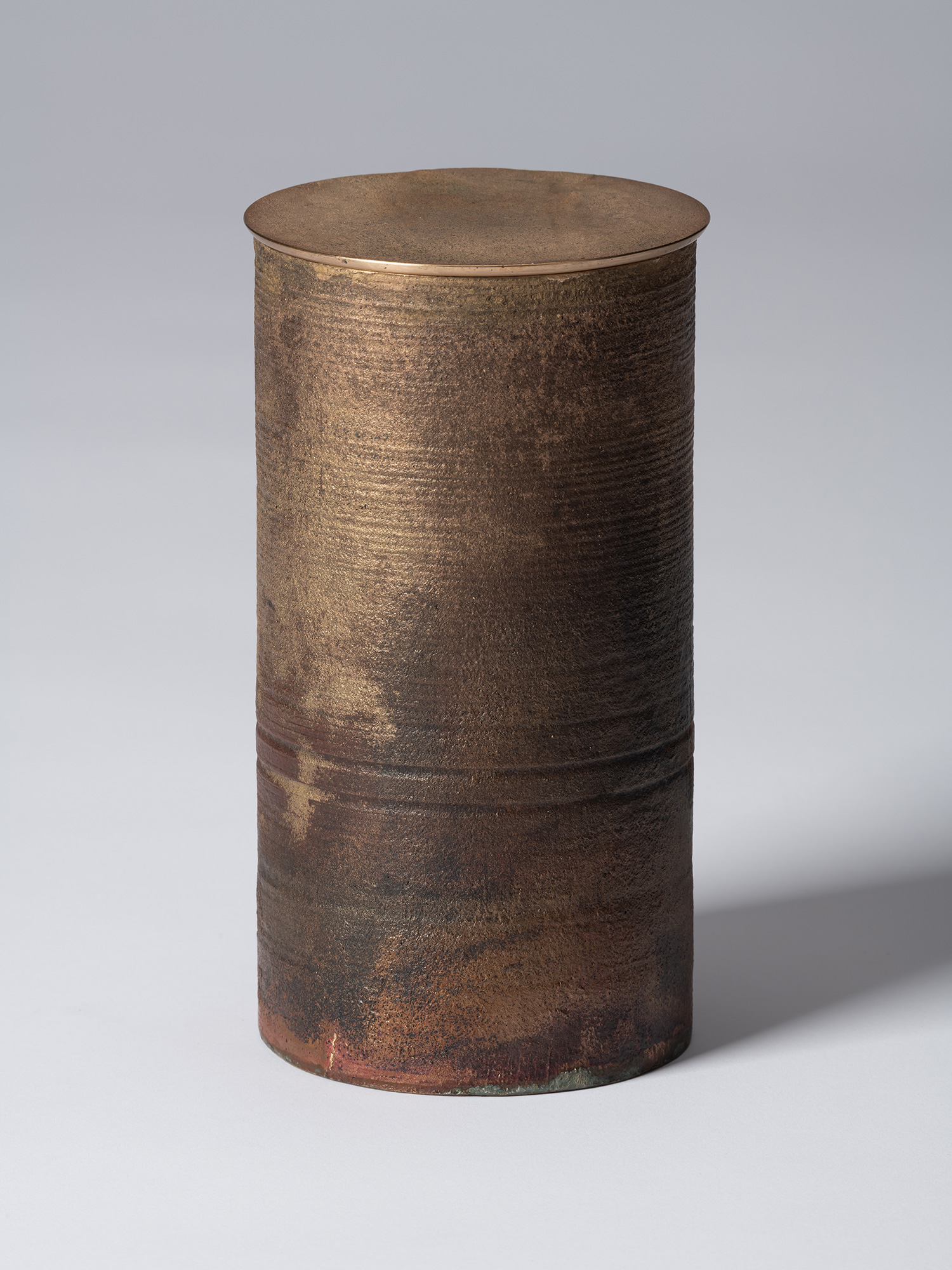 Alternate view of the lidded bronze vessel, showing the cylindrical form and textured exterior...