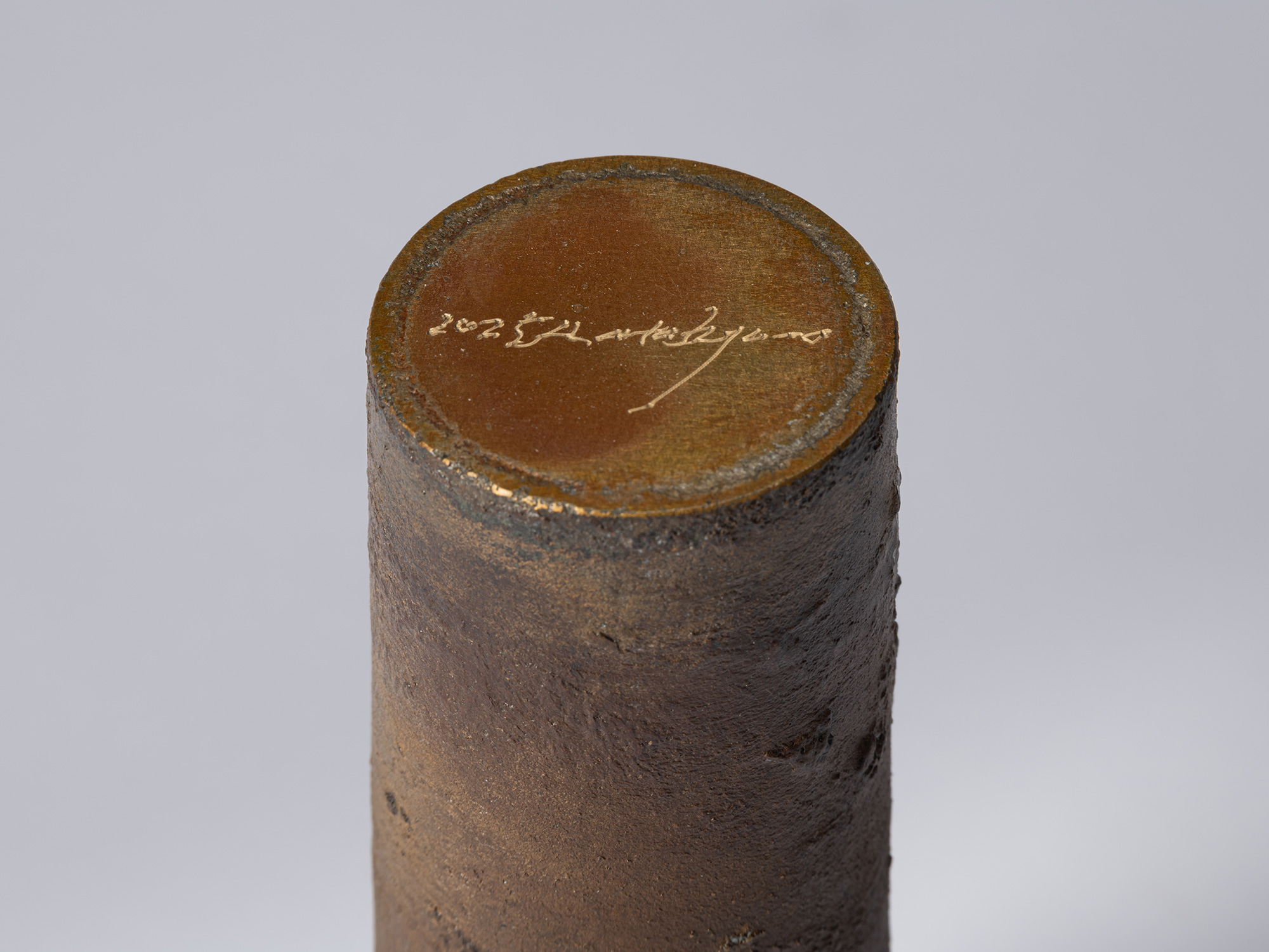 Detail of the underside of the cylindrical bronze vessel, showing a circular base with the artist’s...