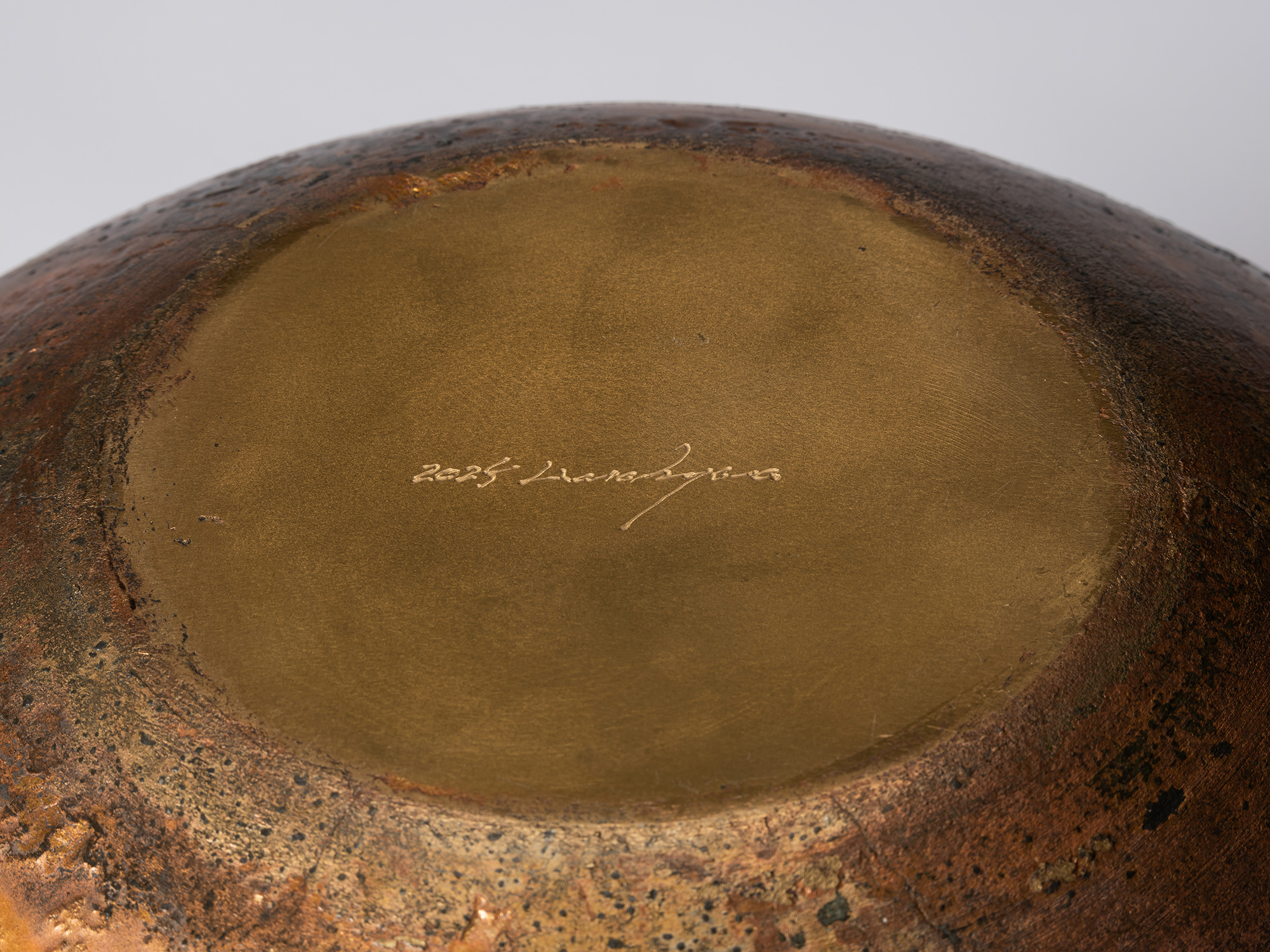 Detail of the vessel’s base, showing the smooth gold-toned circular surface with the artist’s incised...