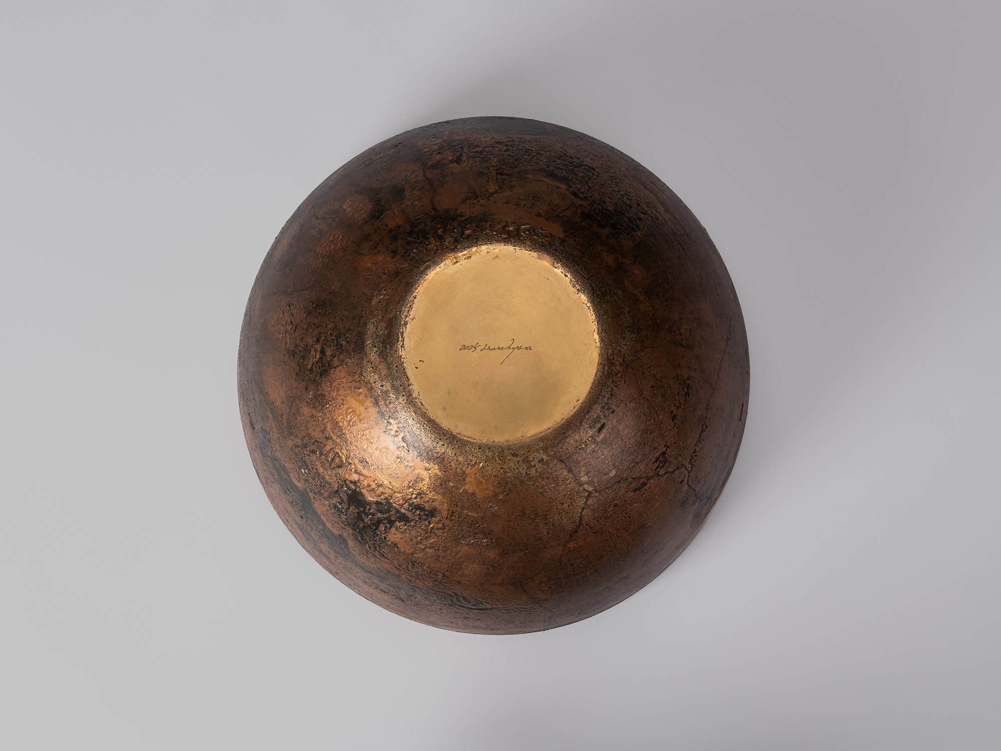 Underside view of the bronze vessel, showing the rounded, heavily mottled exterior surrounding...